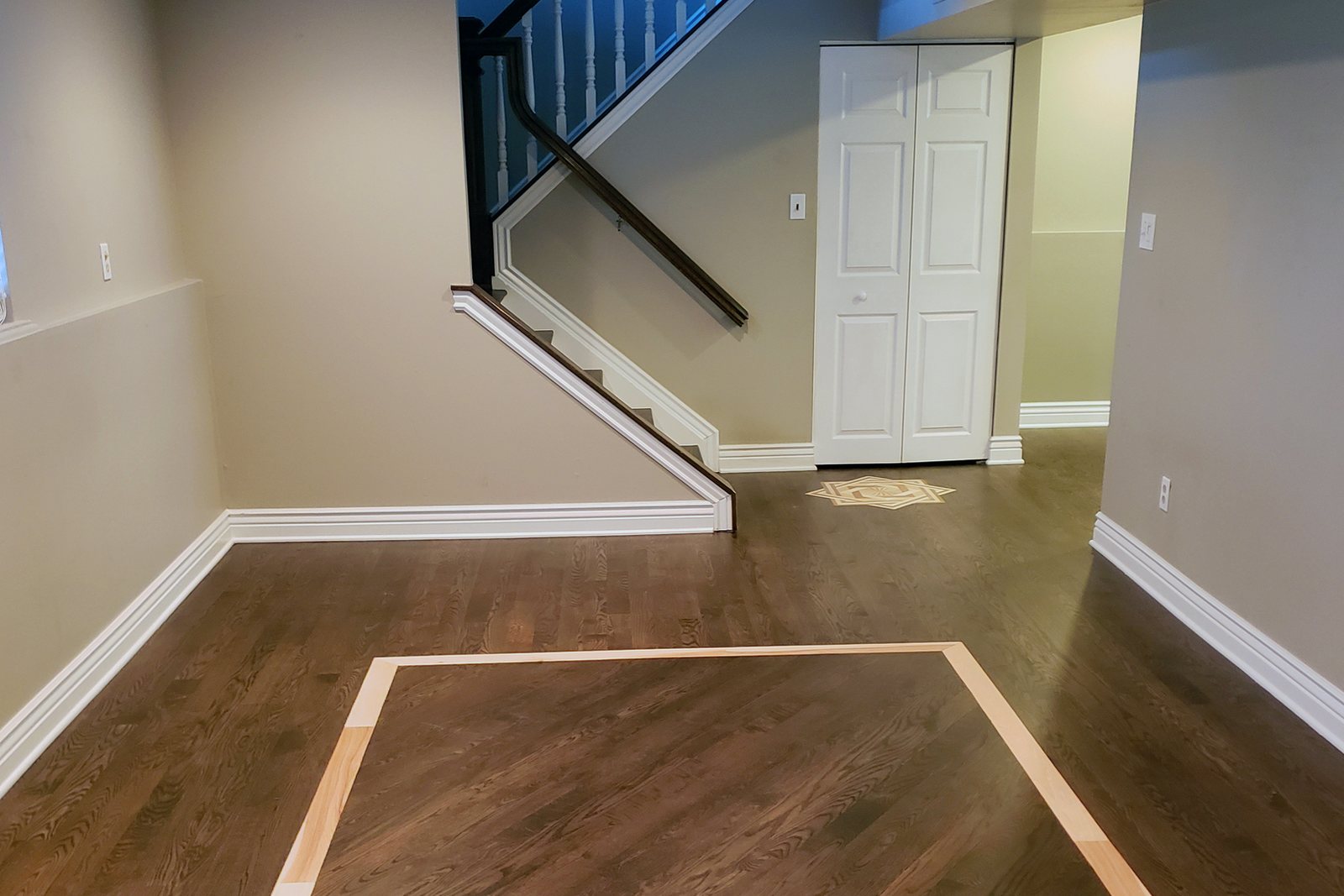 Dark hardwood floor with an inlaid border by a staircase